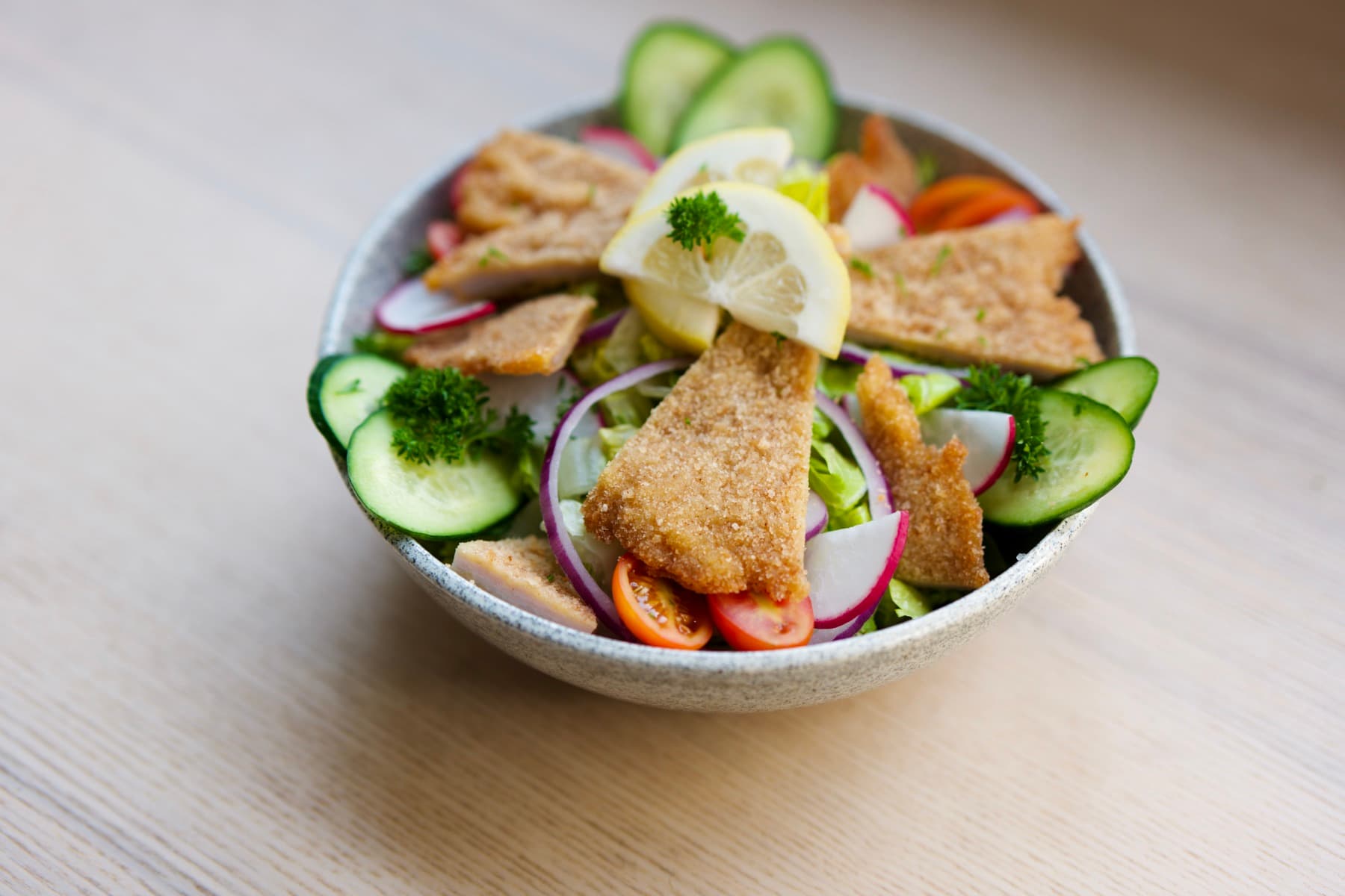 Fresh salad bowl topped with crispy schnitzel strips and lemon