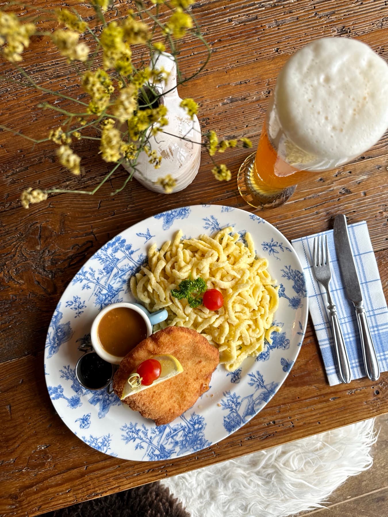 Schnitzel with spätzle on a blue floral plate, served with a cold wheat beer on a rustic wooden table